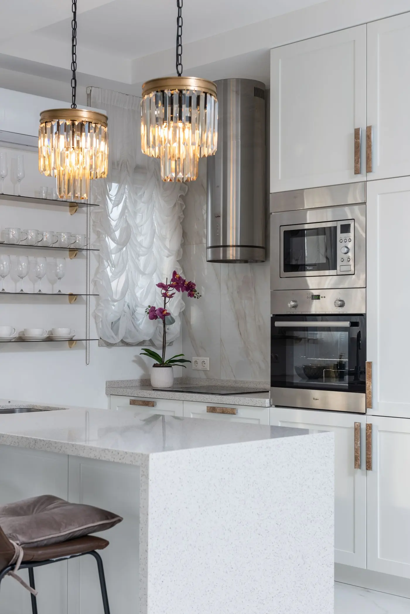 Elegant, spotless white kitchen with a marble island and crystal pendant lights